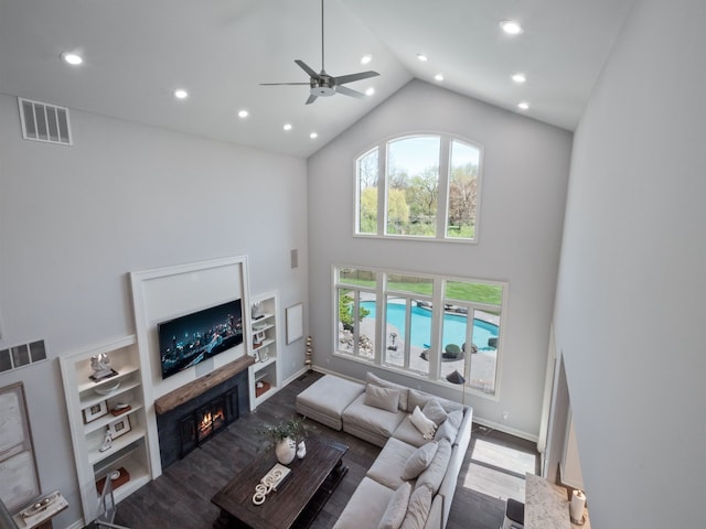 living area with visible vents, wood finished floors, a warm lit fireplace, high vaulted ceiling, and recessed lighting