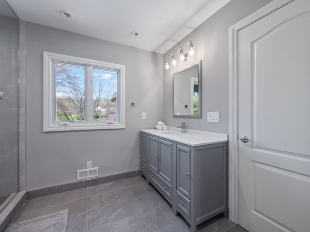 bathroom with baseboards, visible vents, a tile shower, and vanity