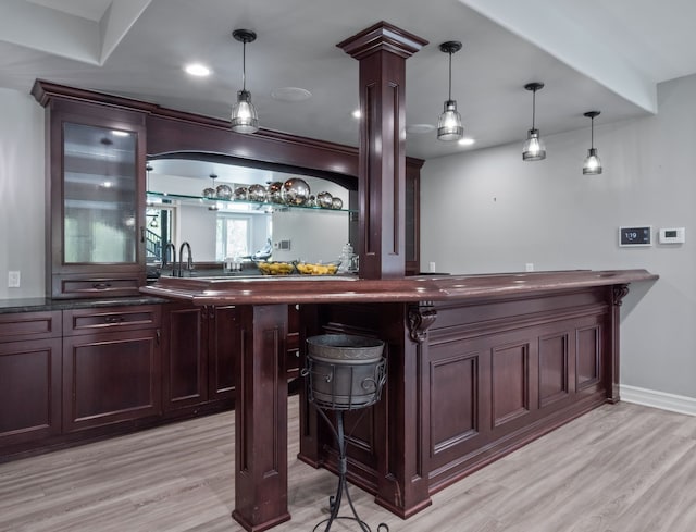 bar with light wood-style floors, bar, and decorative light fixtures