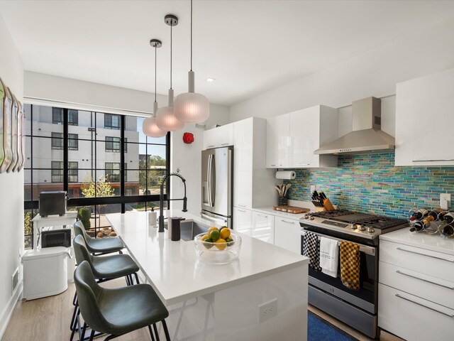 kitchen featuring wall chimney range hood, appliances with stainless steel finishes, a sink, white cabinetry, and backsplash