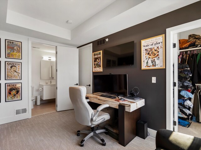home office with light colored carpet, a tray ceiling, visible vents, and a sink