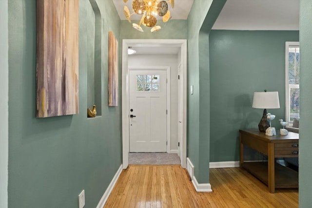 foyer entrance with arched walkways, baseboards, a notable chandelier, and light wood-type flooring