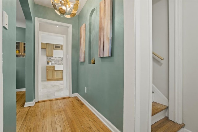 hallway featuring light wood-style floors, baseboards, and a chandelier