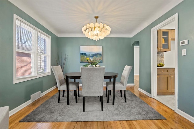 dining area featuring arched walkways, baseboards, visible vents, and light wood-style flooring