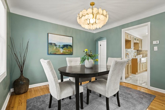 dining space with light wood-style floors, arched walkways, baseboards, and a notable chandelier