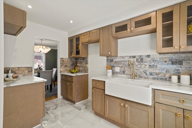 kitchen featuring decorative backsplash, glass insert cabinets, light countertops, brown cabinets, and a sink