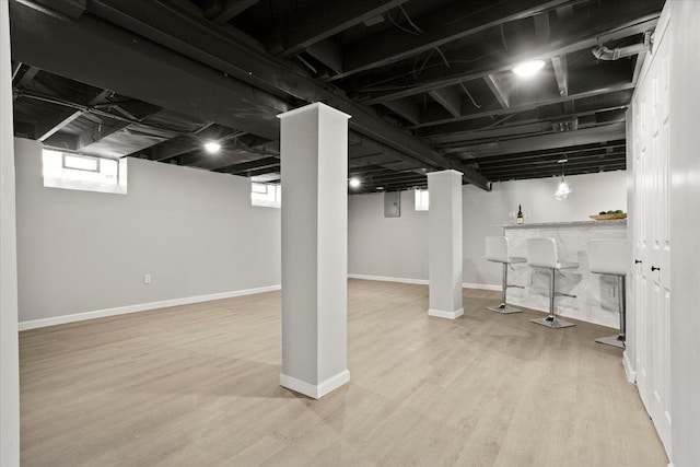 basement featuring a bar, baseboards, and wood finished floors