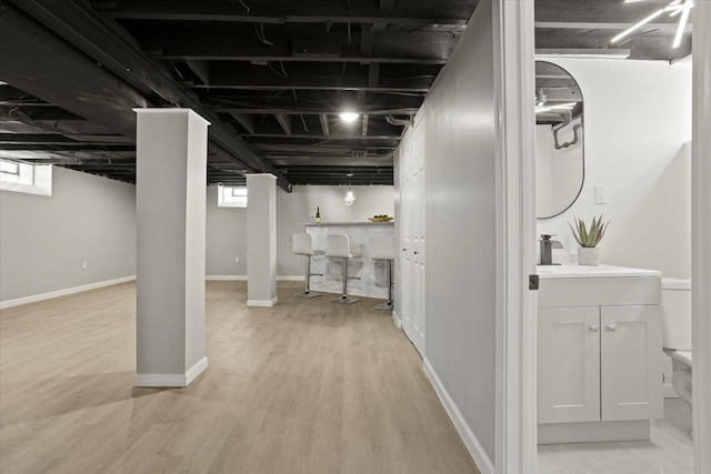 below grade area featuring light wood-style floors, bar area, baseboards, and a sink