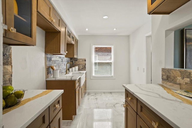 kitchen with glass insert cabinets, light stone counters, decorative backsplash, and marble finish floor