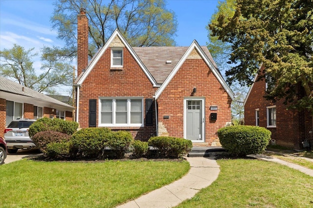 tudor home with brick siding, a front yard, and a chimney