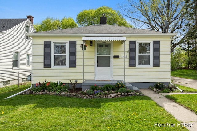 bungalow-style house featuring roof with shingles, a chimney, and a front yard