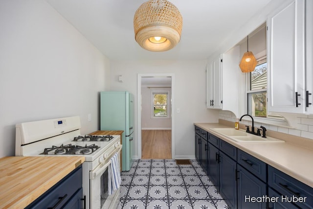 kitchen featuring blue cabinetry, a sink, white cabinets, wood counters, and white appliances
