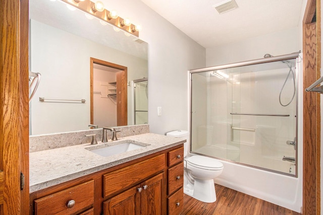 bathroom featuring visible vents, vanity, wood finished floors, toilet, and bath / shower combo with glass door