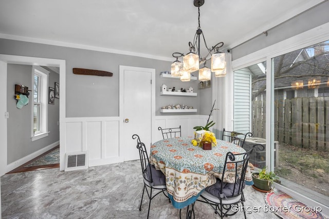 dining space with visible vents, crown molding, a wainscoted wall, a notable chandelier, and a decorative wall