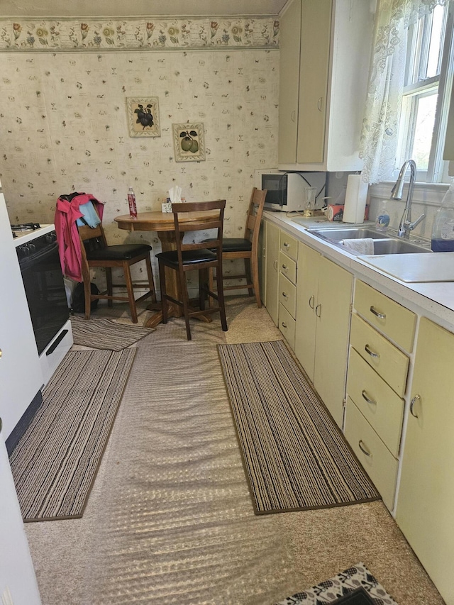 kitchen with cream cabinets, a sink, light countertops, wallpapered walls, and gas range oven