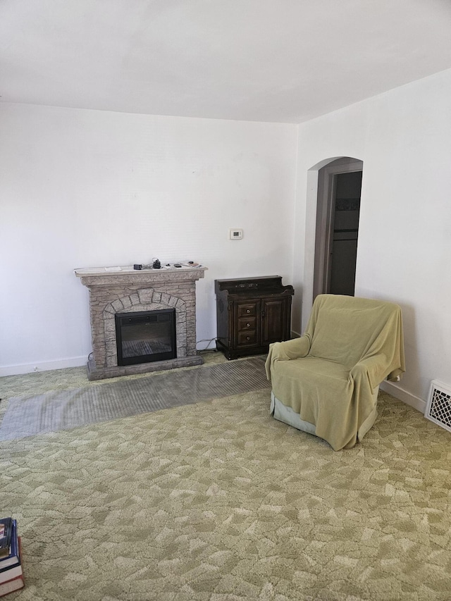 carpeted living room featuring arched walkways, baseboards, visible vents, and a fireplace