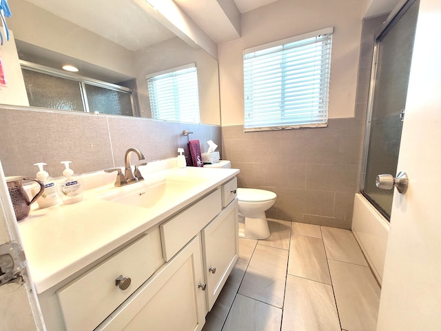 full bath featuring tile walls, vanity, tile patterned floors, combined bath / shower with glass door, and toilet