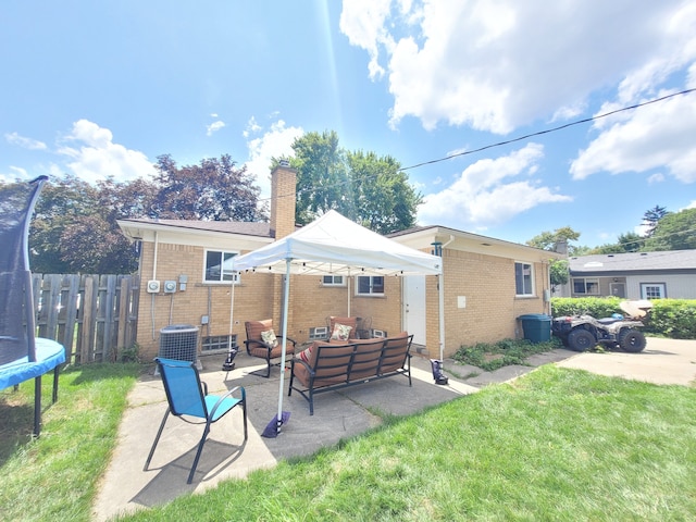 rear view of house with outdoor lounge area, fence, a patio, brick siding, and a trampoline