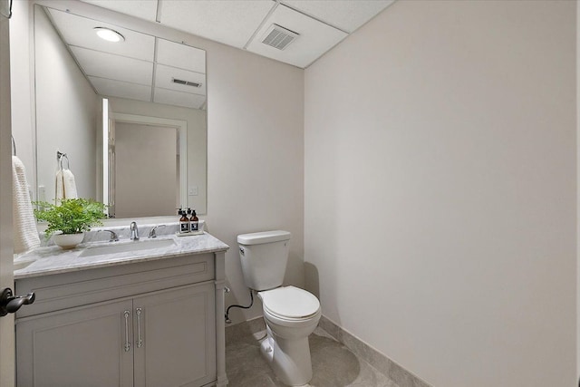 half bath with visible vents, a drop ceiling, toilet, and vanity