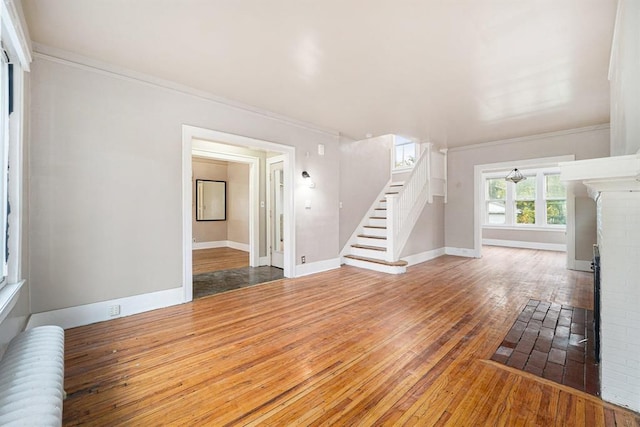 unfurnished living room with wood-type flooring, radiator, stairway, baseboards, and ornamental molding