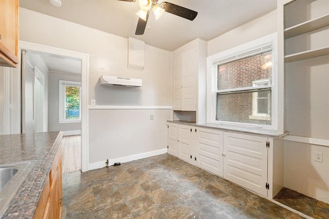 kitchen with under cabinet range hood, baseboards, stone finish flooring, ceiling fan, and a sink