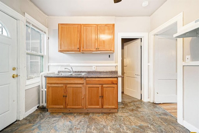 kitchen with baseboards, stone finish floor, brown cabinets, and a sink