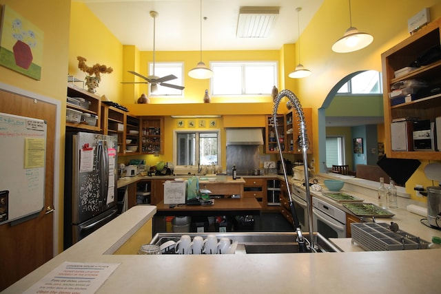 kitchen featuring a ceiling fan, a towering ceiling, freestanding refrigerator, glass insert cabinets, and oven
