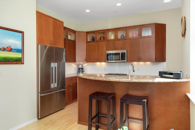 kitchen featuring a peninsula, light stone countertops, light wood-style floors, brown cabinets, and stainless steel appliances