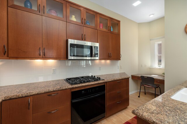 kitchen featuring light wood finished floors, black oven, stainless steel microwave, gas stovetop, and backsplash