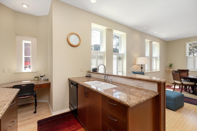 kitchen with a sink, light stone counters, light wood finished floors, a peninsula, and black dishwasher