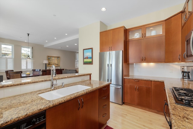 kitchen with brown cabinetry, light stone countertops, a sink, black appliances, and light wood-style flooring