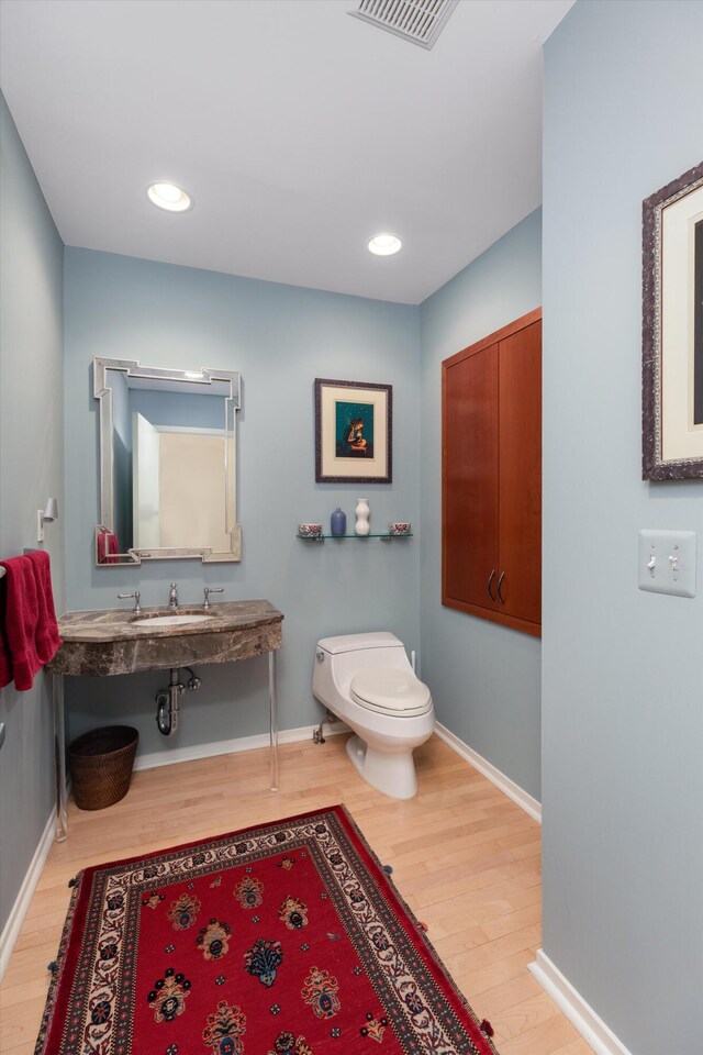 half bath with baseboards, wood finished floors, visible vents, and toilet