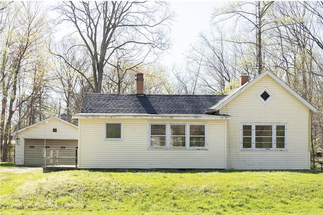 back of house with a lawn, a shingled roof, a chimney, and an outdoor structure