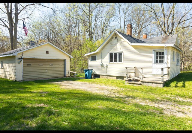 rear view of house featuring an outdoor structure, a garage, a lawn, and a chimney