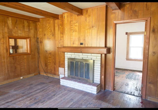unfurnished living room featuring a brick fireplace, beamed ceiling, wood walls, and hardwood / wood-style flooring