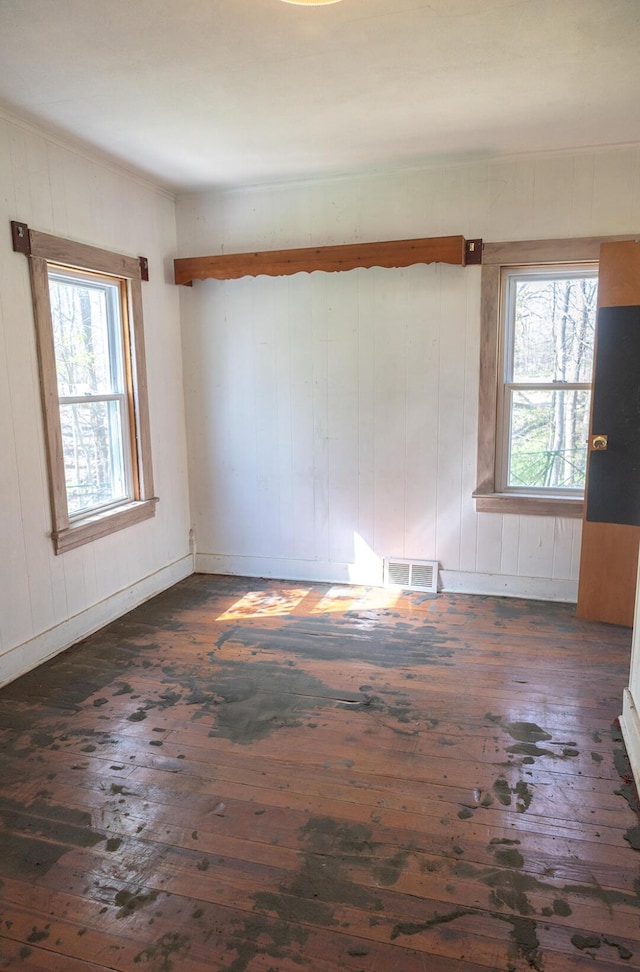 unfurnished room with visible vents, wood walls, dark wood finished floors, and a wealth of natural light