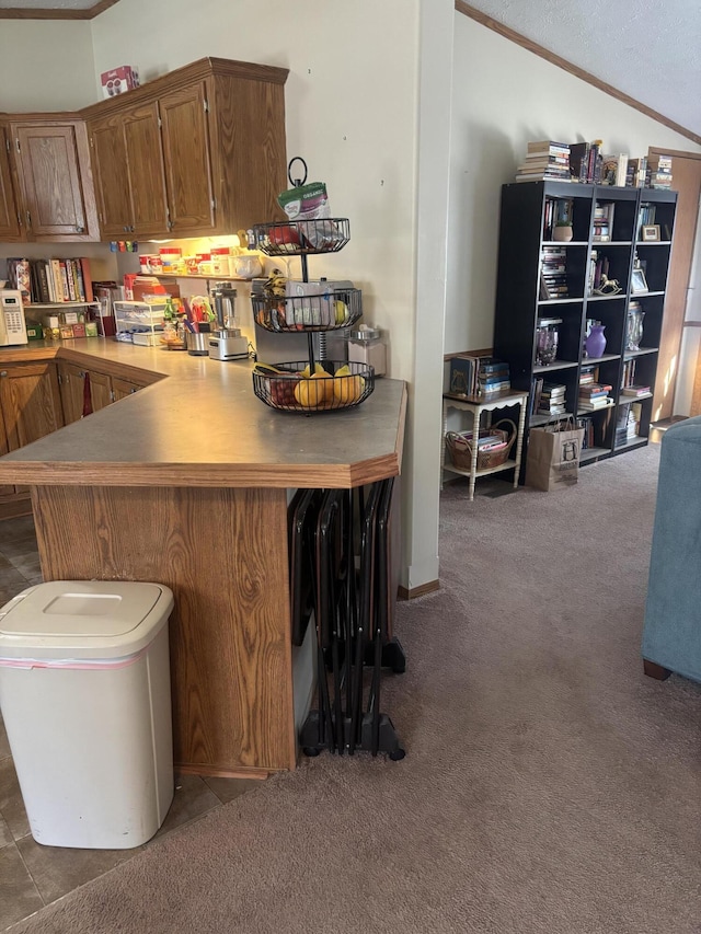 kitchen with crown molding, a peninsula, brown cabinets, carpet, and vaulted ceiling
