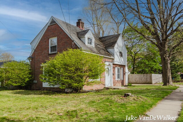 view of side of home with fence, a chimney, a yard, and brick siding