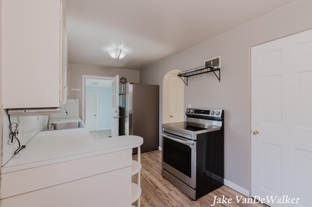 kitchen featuring arched walkways, a sink, light countertops, light wood-style floors, and stainless steel appliances