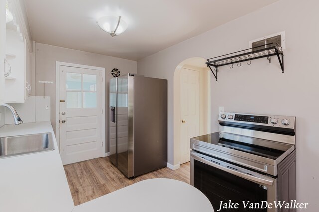 kitchen featuring light wood-type flooring, light countertops, arched walkways, a sink, and appliances with stainless steel finishes