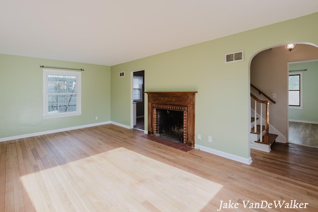 unfurnished living room featuring arched walkways, visible vents, a healthy amount of sunlight, and hardwood / wood-style floors
