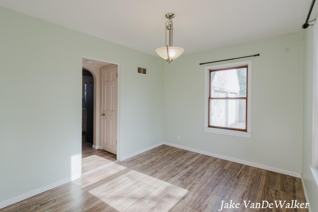 unfurnished room with arched walkways, baseboards, visible vents, and wood finished floors