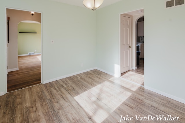 unfurnished room with visible vents, arched walkways, and wood finished floors