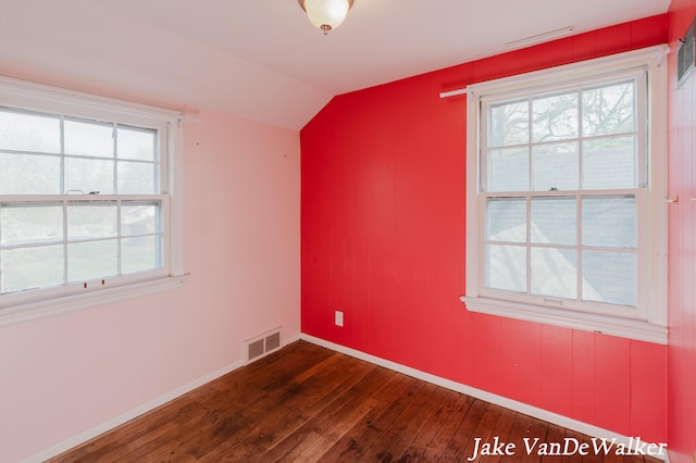 spare room with vaulted ceiling, a wealth of natural light, dark wood-type flooring, and visible vents