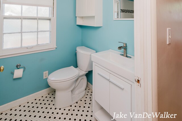 half bath with baseboards, vanity, and toilet