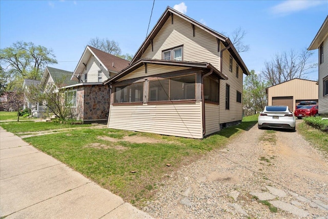 view of front of house featuring a garage, a sunroom, a front yard, an outbuilding, and driveway
