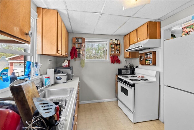 kitchen featuring white appliances, baseboards, a drop ceiling, light floors, and under cabinet range hood