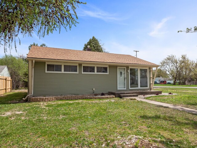ranch-style house featuring fence, a shingled roof, and a front lawn