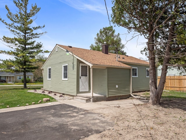exterior space with a lawn, a shingled roof, fence, and a chimney