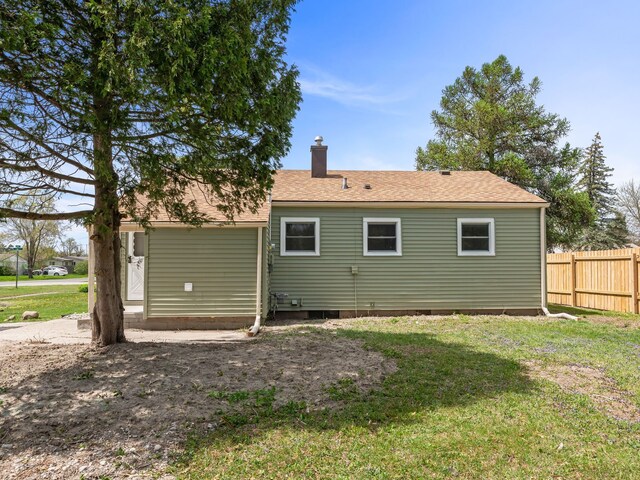 back of property featuring fence, a chimney, a lawn, and a shingled roof